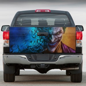 Puede incluir: Una camioneta negra con un gráfico personalizado del Joker de Batman en la puerta trasera. El gráfico es un primer plano de la cara del Joker con un fondo azul y verde.