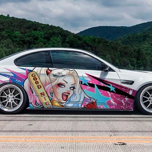 May include: White sports car with custom graphics featuring a cartoon character with the text "GOOD NIGHT" on a baseball bat. The car has a black spoiler and silver rims, parked on a road with a mountain backdrop.