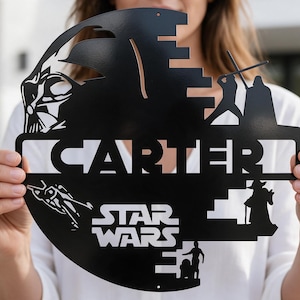 Könnte beinhalten: Ein rundes Wand-Schild aus schwarzem Metall mit einem lasergeschnittenen Design von Star Wars-Figuren wie Darth Vader, Yoda und R2-D2, wobei der Name CARTER mittig und das Star Wars-Logo am unteren Rand zu sehen sind.