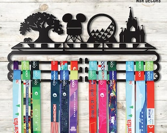 May include: Black metal medal display rack featuring silhouettes of a tree, Mickey Mouse, a Ferris wheel, and a castle. Colorful marathon ribbons hang below. The text "NSR DECORS" is at the top.