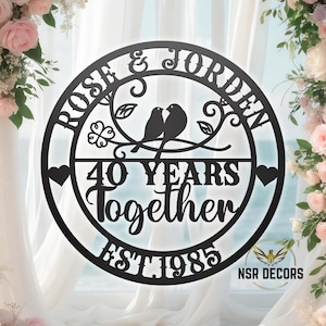 Puede incluir: Placa redonda de metal negro con los nombres "Rose & Jordan" y el texto "40 Years Together Est 1985" con un dise&ntilde;o de dos p&aacute;jaros en una rama con hojas.