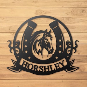 Pode incluir: Ferradura de metal preto com a cabeça de um cavalo no seu interior e uma faixa com o nome "HORSHLEY" por baixo. A ferradura é rodeada por volutas decorativas.
