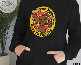 May include: Black unisex hoodie with a yellow circle graphic featuring a cartoon Bigfoot doing kung fu. The text inside the circle reads "Even Bigfoot Has Kung Fu Fighting."