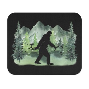 May include: A black silhouette of Bigfoot walking through a watercolor forest scene with green trees and mountains.