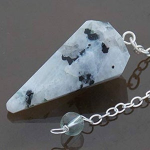 May include: A white and black gemstone pendulum with a silver chain and a green crystal bead.