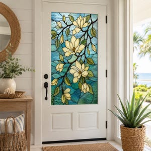 May include: A white door featuring a tall, rectangular stained glass window panel. The glass displays a botanical design of cream-colored magnolia flowers and green leaves set against a textured background of varying shades of blue and teal.