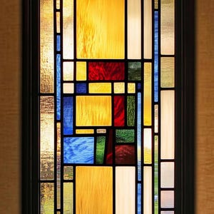 Op de afbeelding: Een rechthoekig glas-in-loodraam met een zwart frame. Het ontwerp toont een geometrisch patroon van gekleurde glazen panelen, waaronder geel, rood, blauw, groen en wit. Het glas heeft zowel getextureerde als gladde secties.