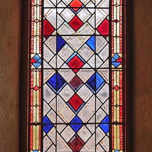 May include: A stained glass window featuring a geometric design of red, blue and white diamonds. The window is framed in wood and has a border of yellow and orange.