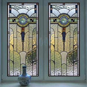 May include: Two stained glass windows with an Art Nouveau design. The windows feature a symmetrical pattern with a central circular motif in shades of blue, green, and yellow. A decorative vase with blue floral patterns sits on the windowsill.