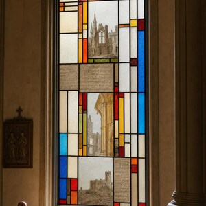 May include: A rectangular stained glass window featuring a geometric grid of clear, blue, red, and yellow panels. Three central panels contain detailed architectural sketches of stone buildings, while two panels display blocks of handwritten text.