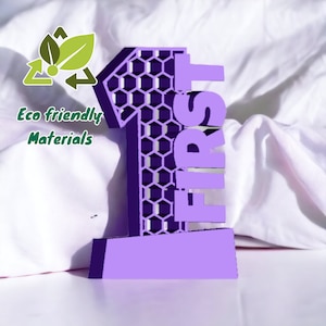 Puede incluir: Un número uno lila impreso en 3D con la palabra "FIRST" apilada verticalmente. El número uno tiene un patrón de panal. La imagen también incluye un gráfico verde y blanco con el texto "Eco friendly Materials."