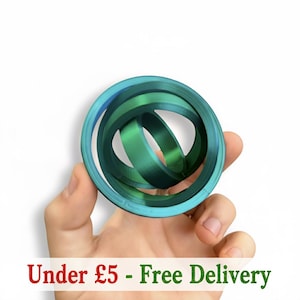 Puede incluir: Una escultura de anillos entrelazados en verde y turquesa. La escultura se sostiene en una mano sobre un fondo blanco. El texto "Under £5 - Free Delivery" está en la parte inferior de la imagen.