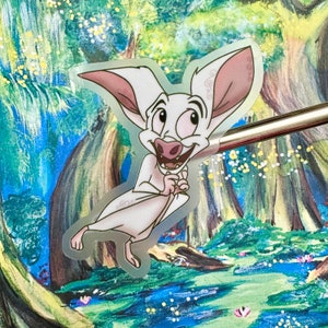 以下が含まれることがあります： 緑と青の色合いの森が描かれた背景に、ピンクの耳と大きな笑顔をした白い漫画の蝙蝠が描かれている。