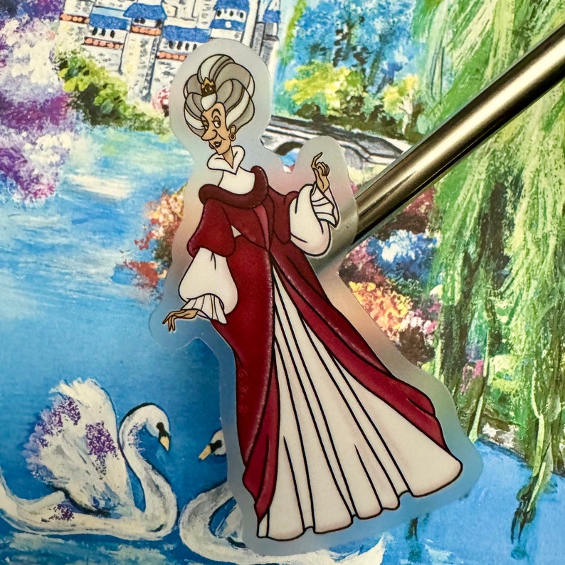 Op de afbeelding: Een transparante sticker met een cartoonillustratie van een oudere vrouw met grijs haar die een rood-witte jurk en een kroon draagt. De sticker bevindt zich op een blauwe en groene achtergrond met een witte zwaan.