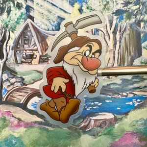 Könnte beinhalten: Ein mürrisch aussehender Comic-Zwerg mit weißem Bart und rotem Hemd hält eine Spitzhacke. Er trägt einen braunen Hut und hat eine rote Nase. Der Hintergrund ist eine Comic-Waldszene.
