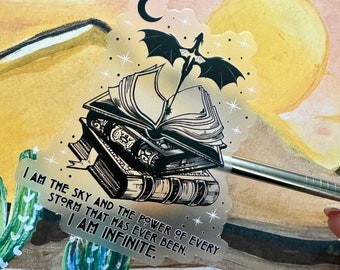 May include: A silver holographic sticker with a black and white illustration of a dragon flying over a stack of books. The sticker has the text "I am the sky and the power of every storm that has ever been. I am infinite."
