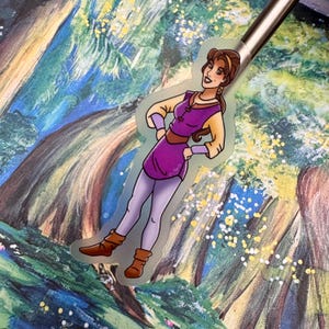 May include: A sticker featuring a cartoon woman with brown hair, wearing a purple and yellow outfit, standing with her hands on her hips. The background is a watercolor painting of a forest.