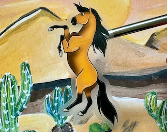 May include: A clear sticker of a brown and black horse with a long mane and tail, standing on its hind legs. The sticker is on a background of a painted landscape with a yellow sun and green cacti.