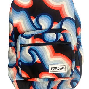 May include: A backpack with a vibrant, wavy pattern in shades of red, blue, and white against a black background. The backpack has a front pocket with a zipper and a white label that reads "SAROWA".