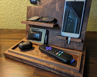 May include: A wooden organizer with a phone stand, watch holder, glasses holder, and a tray for keys or other small items. The organizer is made of dark wood and has a natural finish. The phone stand is made of metal and has a black finish. The watch holder is made of metal and has a silver finish. The glasses holder is made of metal and has a black finish. The tray is made of wood and has a natural finish.