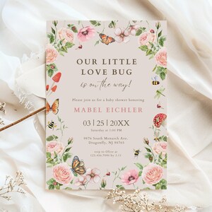 Puede incluir: Invitación a un baby shower con ilustraciones florales y de mariposas. El texto dice "Our Little Love Bug is on the way!" con detalles para el baby shower de Mabel Eichler. El diseño presenta rosas rosas, mariposas y la fecha.