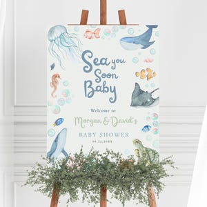 Può includere: Un cartello di benvenuto per il baby shower con illustrazioni ad acquerello di vita marina, tra cui una balena, una medusa e un cavalluccio marino. Il cartello recita "Sea you Soon Baby" e dà il benvenuto al baby shower di Morgan & David.