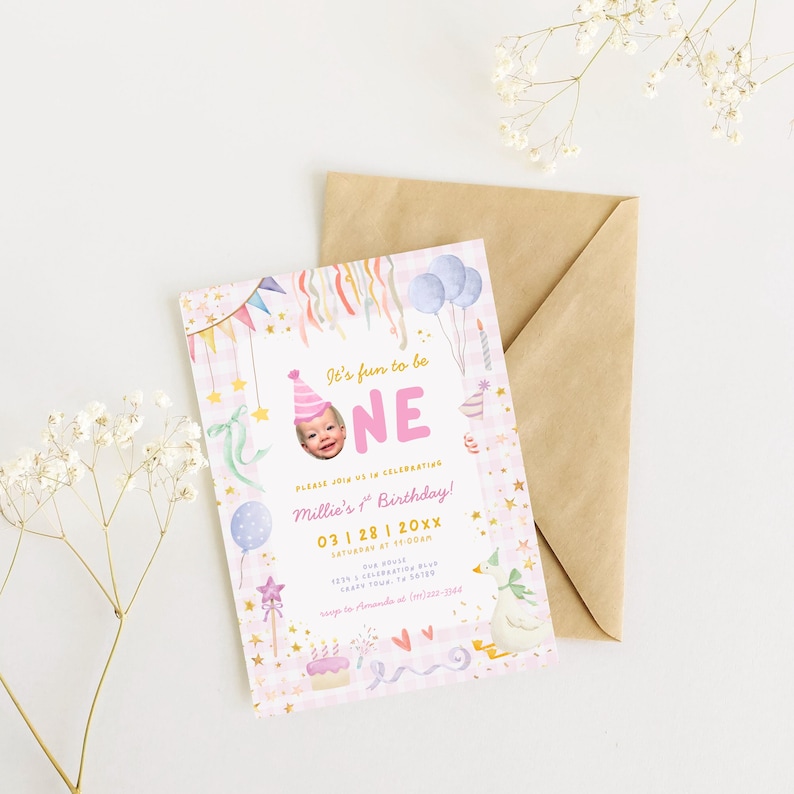 May include: A pink and white birthday invitation with the text "It's fun to be ONE" and a photo of a baby. The invitation includes decorative elements like balloons, stars, and a cake, with a brown envelope in the background.