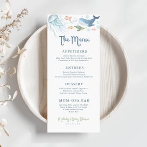 May include: A menu card with a watercolor illustration of marine life, including a jellyfish, whale, and fish. The menu lists appetizers, entrees, dessert, and a Mom-osa bar. The text reads "Melody's Baby Shower" and the date.