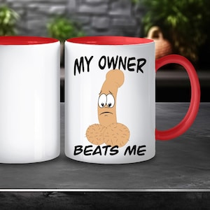 以下が含まれることがあります： 赤色の内側とハンドルが付いた白いセラミックマグ。マグには、悲しいペニスの漫画イラストと黒い文字で「MY OWNER BEATS ME」が描かれています。マグは暗い表面に表示されています。