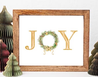 May include: A framed print with the word "JOY" in gold lettering, with a wreath in place of the "O". Decorative paper Christmas trees in various colors surround the frame, creating a festive holiday scene.