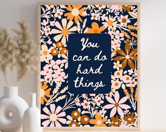 May include: A framed print with a navy blue background and a floral pattern in shades of pink, orange, and white. The text "You can do hard things" is written in white on a dark blue rectangle in the center of the print.