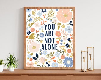 May include: A framed print with a floral pattern in shades of blue, pink, and green. The text "YOU ARE NOT ALONE" is printed in navy blue.