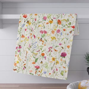 May include: A white kitchen towel with a floral pattern featuring a variety of colorful flowers, butterflies, and bees. The towel is hanging on a white shelf in a kitchen setting.