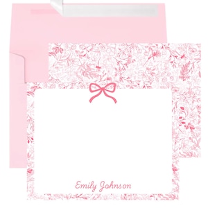 May include: A stationery set featuring a pink envelope and a matching card. The card has a white center with a pink floral border and a pink bow. The name "Emily Johnson" is printed in pink script on the card.