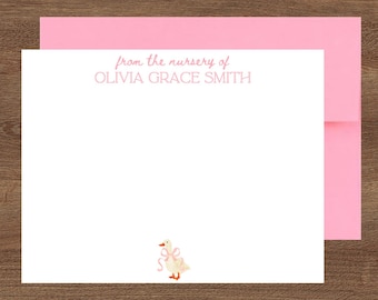 May include: White stationery with a pink envelope. The stationery features the text "from the nursery of OLIVIA GRACE SMITH" in pink. A watercolor illustration of a goose with a pink bow is in the bottom corner. The stationery is on a wooden surface.