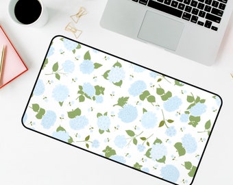 May include: A white desk mat with a repeating pattern of blue hydrangeas and green leaves.