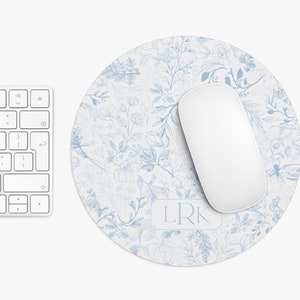 May include: A round blue and white floral mouse pad with the initials "LRK" in a white rectangle in the center. A white wireless mouse is on top of the mouse pad.