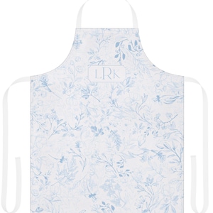 Puede incluir: Un delantal blanco con un estampado floral azul y el monograma "LRK" en un rectángulo blanco.