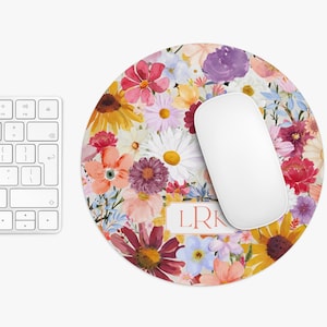 May include: A round floral mouse pad with a white mouse on top. The mouse pad features a colorful floral design with pink, yellow, blue, and purple flowers. The text "LRK" is printed in the center of the mouse pad.