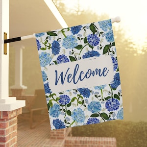 May include: A welcome garden flag with a blue and white floral pattern. The flag features a white banner with the word "Welcome" in blue script.