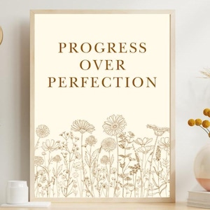 Puede incluir: Una impresión enmarcada beige con el texto "Progress Over Perfection" en letras marrones. La impresión presenta una línea de flores y hojas marrones de contorno.