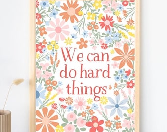 May include: A framed print with a white background and a floral pattern in shades of pink, orange, yellow, blue, and green. The text "We can do hard things" is written in red.