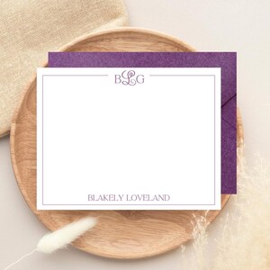 以下が含まれることがあります： 紫色のモノグラムと「Blakely Loveland」の名前が紫で印刷された白い便箋。カードは木製のプレートに置かれ、その背後には紫色の封筒があります。背景にはベージュの布と乾燥した植物が含まれています。