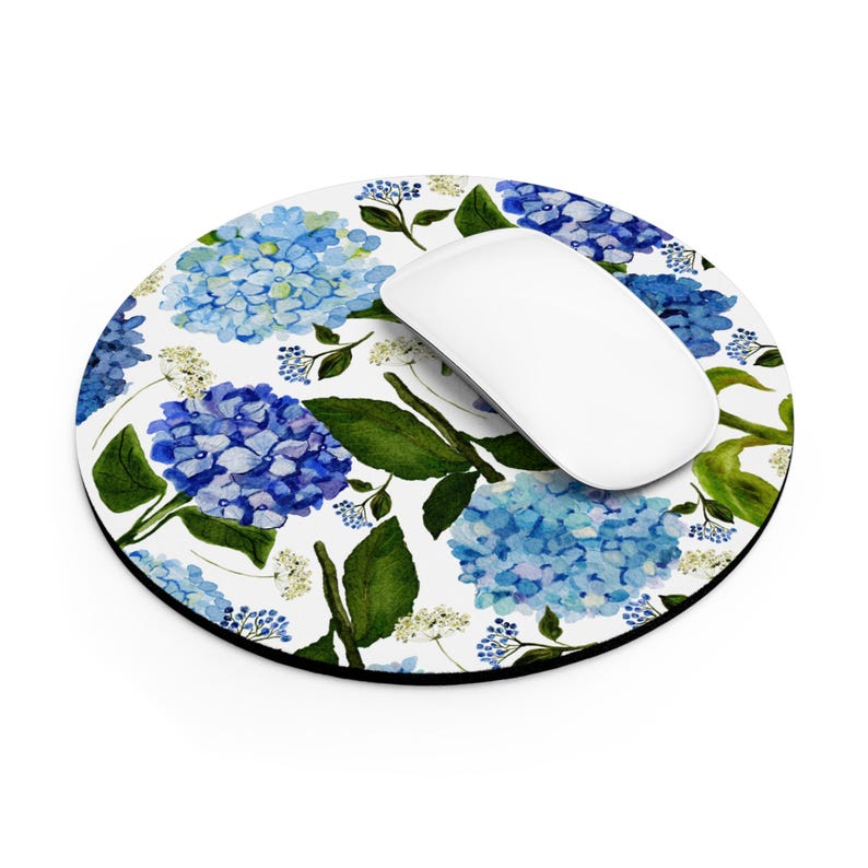 K&ouml;nnte beinhalten: Eine runde Mauspad mit wei&szlig;em Hintergrund und einem blauen und gr&uuml;nen Blumenmuster. Das Muster zeigt Hortensien und Bl&auml;tter. Eine wei&szlig;e Computermaus liegt auf der Mauspad.