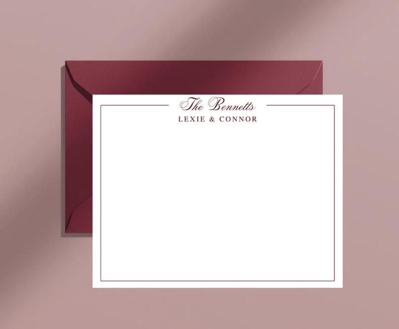 May include: A white stationery card with a burgundy border and the text "The Bennetts Lexie & Connor" in a script font. The card is on top of a burgundy envelope, with a soft pink background.