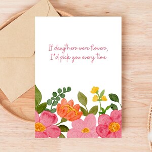 Peut inclure: Une carte de v&oelig;ux blanche avec le texte "If daughters were flowers, I'd pick you every time." La carte pr&eacute;sente des fleurs &agrave; l'aquarelle roses, oranges et jaunes. Une enveloppe repose sur un plateau en bois.