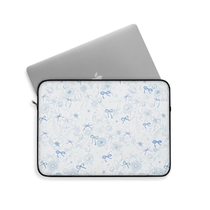 May include: A white laptop sleeve with a blue floral pattern featuring delicate bows and flowers. The sleeve has a zipper closure.