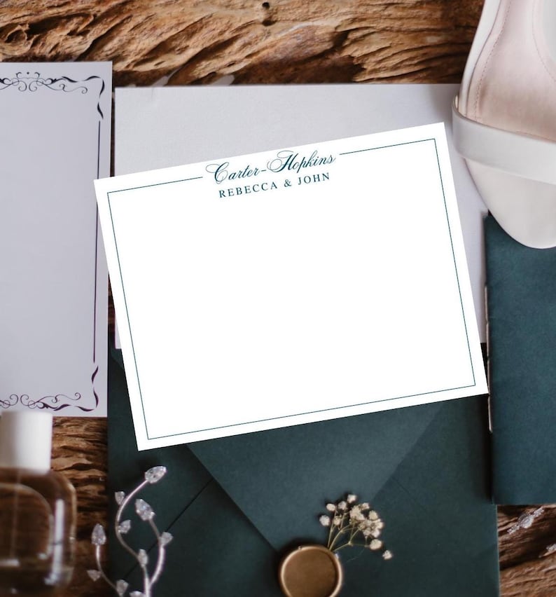 May include: A white stationery card with a teal border and the text "Carter-Hopkins REBECCA & JOHN" is centered on a dark teal envelope. The scene includes a white shoe, a decorative sprig, and a bottle.