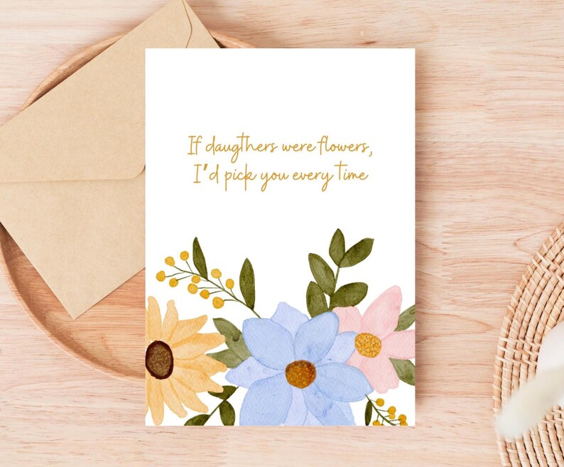 Peut inclure: Carte de v&oelig;ux blanche avec des fleurs &agrave; l'aquarelle jaunes, bleues et roses, et le texte "If daughters were flowers, I'd pick you every time." Une enveloppe en papier kraft est &agrave; c&ocirc;t&eacute; de la carte.