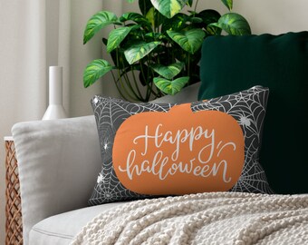 May include: Rectangular Halloween-themed pillow with an orange pumpkin design and the words "Happy Halloween" in white script. The background features a black and white spiderweb pattern. The pillow is on a gray couch.